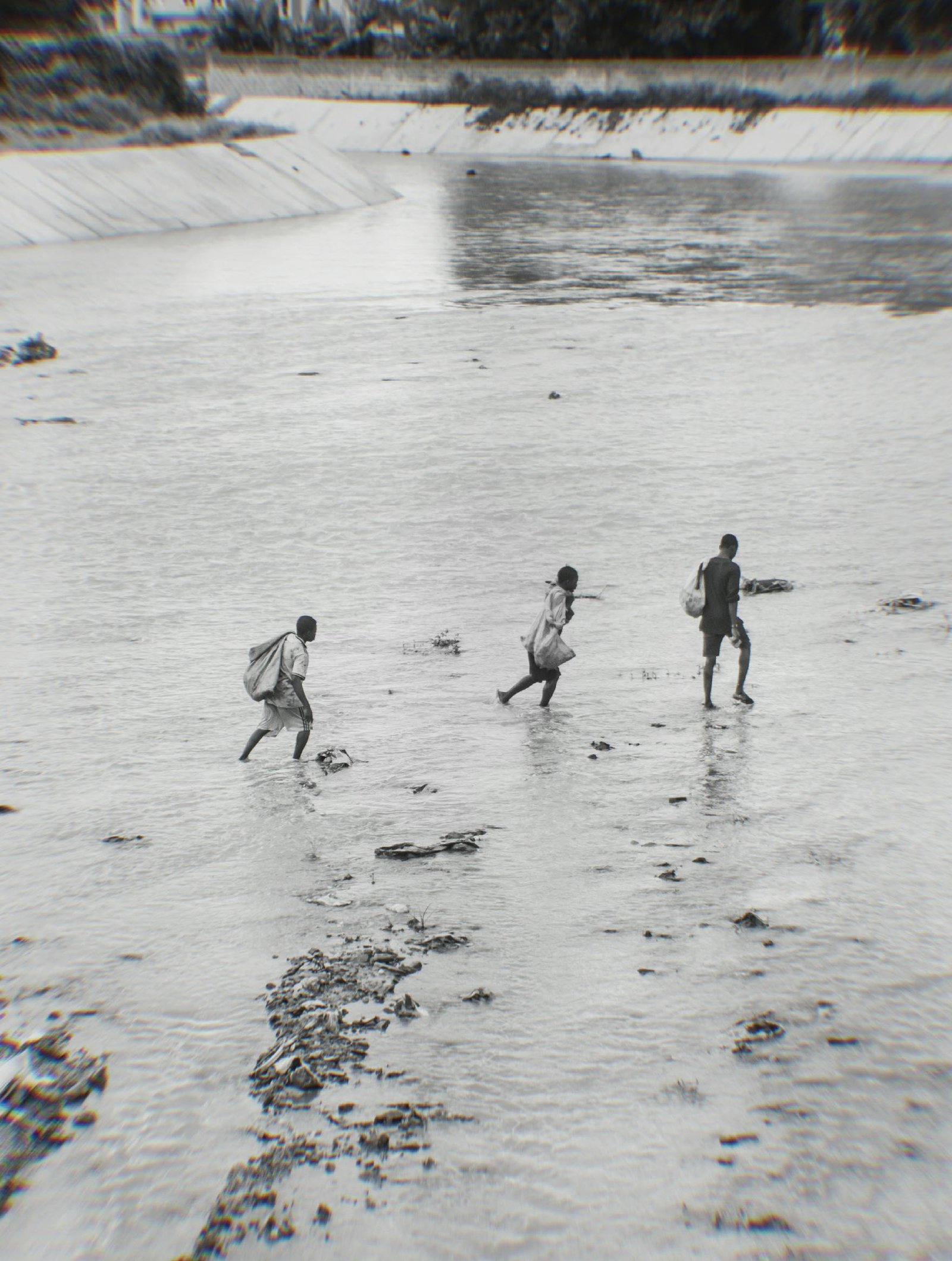 A black and white image of three individuals crossing a shallow, flooded river showing resilience and hope.